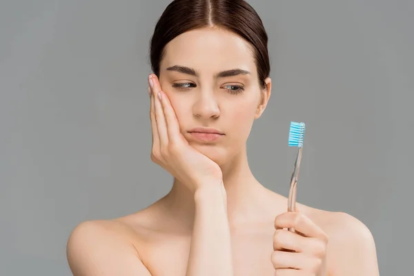 Giovane donna nuda toccare il viso e guardando spazzolino isolato su grigio — Foto stock