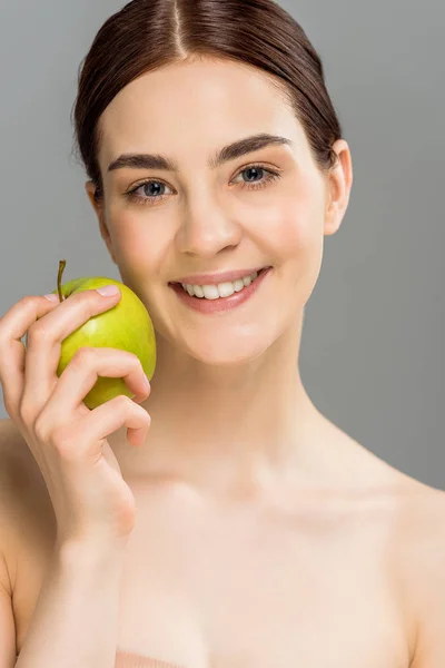 Happy woman smiling while holding green apple isolated on grey — Stock Photo