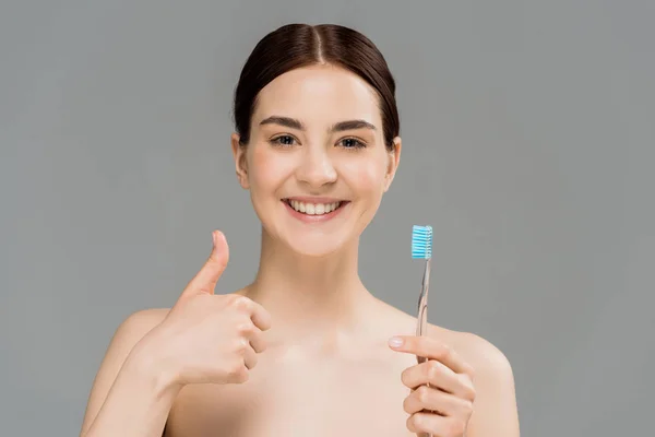 Веселая голая женщина держит зубную щетку, показывая большой палец на серой — стоковое фото