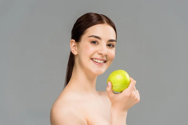Allegra donna nuda sorridente mentre tiene mela verde isolata sul grigio — Foto stock
