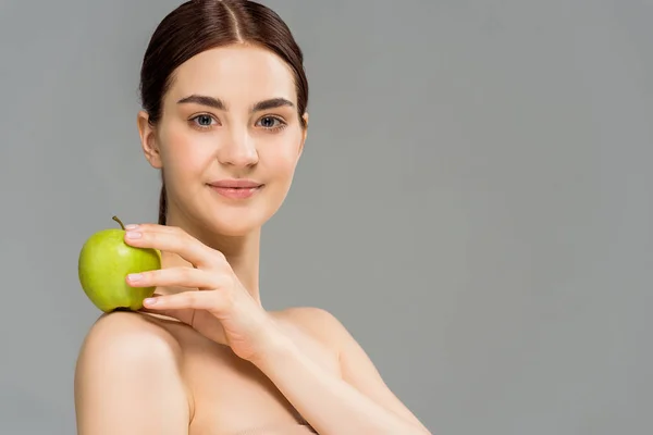 Allegra donna nuda sorridente mentre tiene mela verde isolata sul grigio — Foto stock