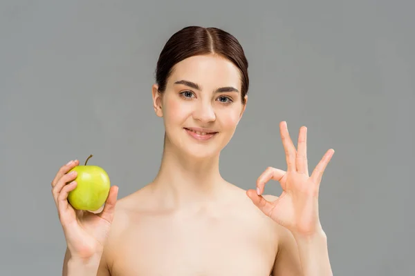 Fröhliche nackte Frau lächelt, während sie grünen Apfel in der Hand hält und Ok-Zeichen zeigt, isoliert auf grau — Stockfoto