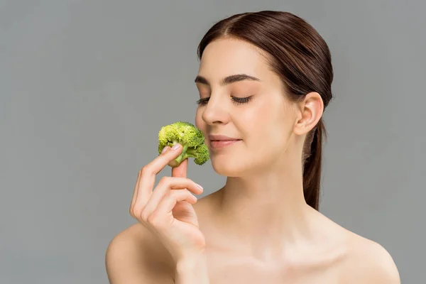 Happy naked woman smiling while holding green broccoli isolated on grey — Stock Photo