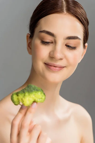 Foco seletivo de mulher nua feliz sorrindo enquanto segurando brócolis verde isolado no cinza — Fotografia de Stock