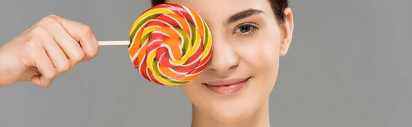 Panoramic shot of cheerful woman covering eye with colorful lollipop isolated on grey — Stock Photo