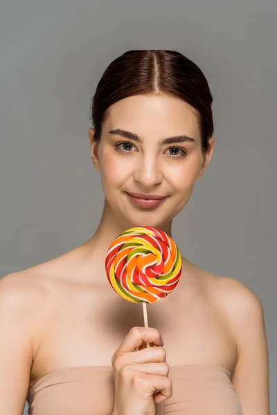 Feliz joven mujer sosteniendo colorido piruleta aislado en gris - foto de stock