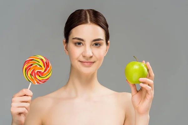 Приваблива гола дівчина тримає зелене яблуко і солодкий льодяник ізольована на сірому — стокове фото