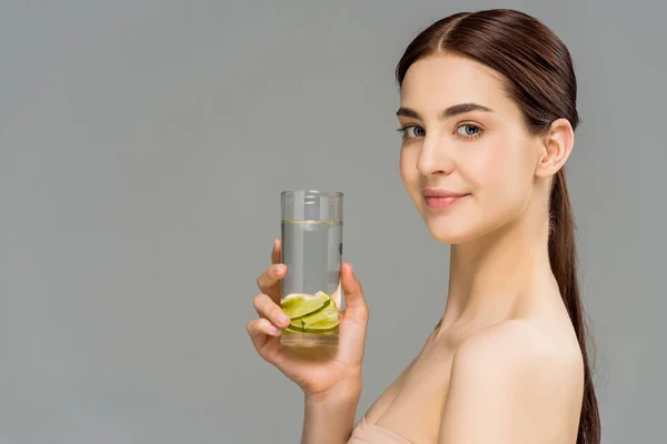 Cheerful young woman holding glass of water with sliced lime isolated on grey — Stock Photo