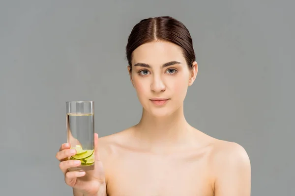 Attraktive junge Frau hält ein Glas Wasser mit geschnittenem Kalk isoliert auf grau — Stockfoto