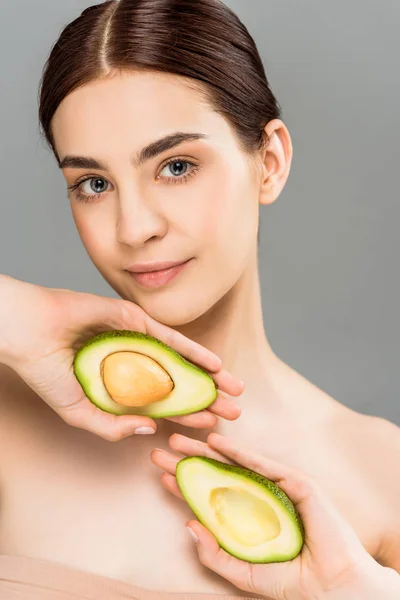 Hermosa joven sosteniendo mitades de aguacate aisladas en gris — Stock Photo