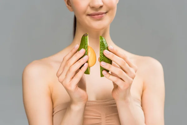 Cropped view of happy young woman holding avocado halves isolated on grey — Stock Photo