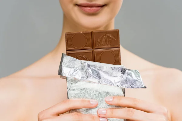 Обрізаний вид веселої молодої жінки, що тримає шоколадний батончик ізольовано на сірому — стокове фото