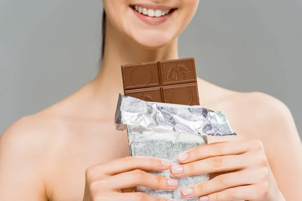 Cropped view of smiling young woman holding chocolate bar isolated on grey — Stock Photo