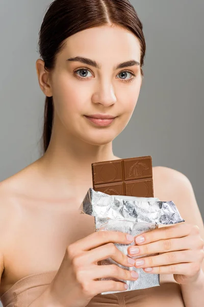 Attractive young woman holding chocolate bar isolated on grey — Stock Photo