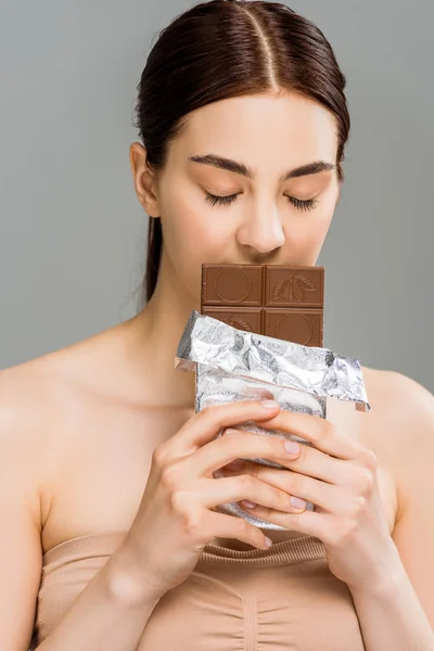 Jeune femme couvrant visage tout en sentant la barre de chocolat isolé sur gris — Photo de stock