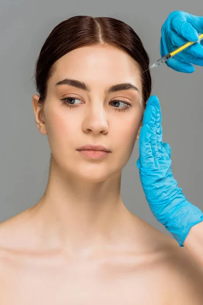 Vista recortada de cirujano plástico haciendo inyección de belleza a mujer desnuda atractiva aislada en gris - foto de stock