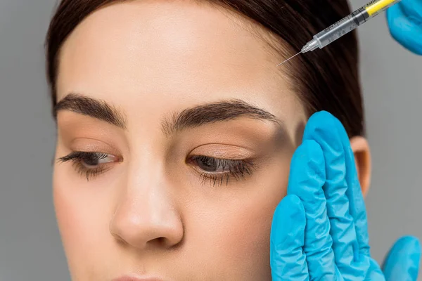 Cropped view of plastic surgeon holding syringe near brunette woman isolated on grey — Stock Photo