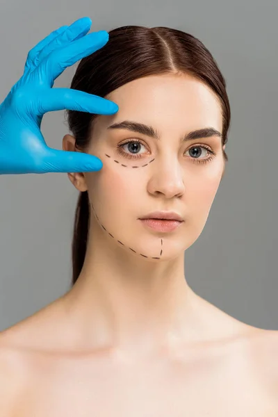 Cropped view of plastic surgeon in latex glove touching face of beautiful naked woman isolated on grey — Stock Photo