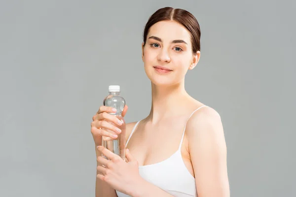 Jovem feliz segurando garrafa com água isolada em cinza — Fotografia de Stock