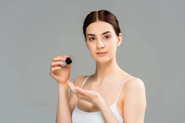 Attractive brunette woman holding pipette and looking at camera isolated on grey — Stock Photo