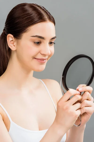 Bonita jovem mulher olhando para o espelho e sorrindo isolado no cinza — Fotografia de Stock