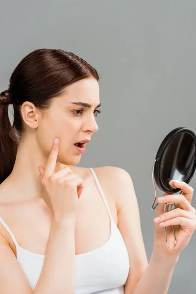Überrascht junge Frau blickt in Spiegel isoliert auf grau — Stockfoto
