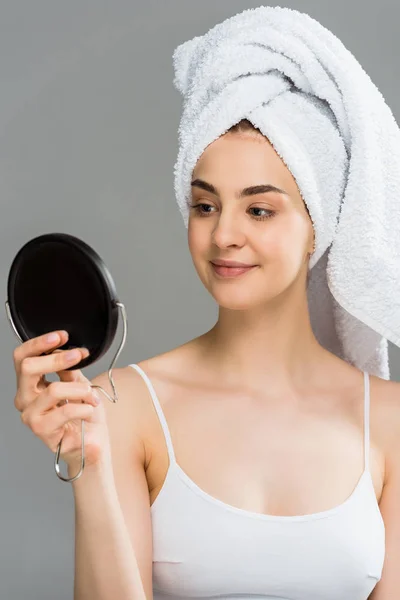 Glückliche junge Frau mit Handtuch auf dem Kopf, Blick auf Spiegel isoliert auf grau — Stockfoto