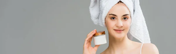 Tiro panorâmico de mulher alegre com toalha na cabeça segurando recipiente com creme cosmético isolado em cinza — Fotografia de Stock
