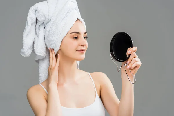 Beautiful young woman with towel on head looking at mirror isolated on grey — Stock Photo