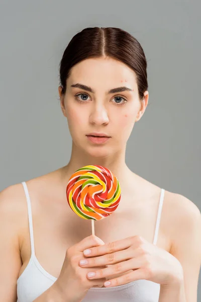 Брюнетка жінка з прищами на обличчі тримає солодкий льодяник ізольовано на сірому — стокове фото