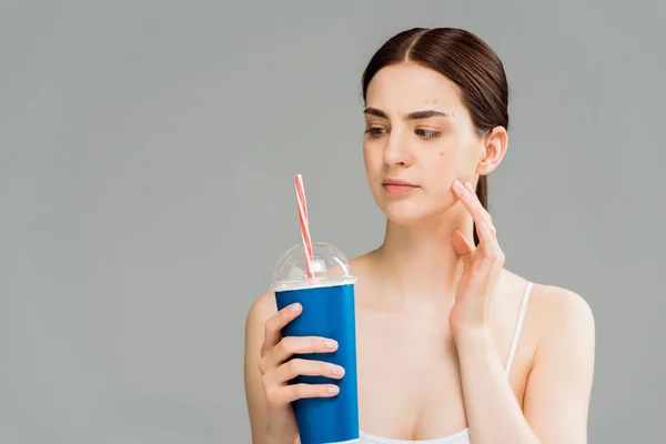 Frau mit Akne im Gesicht sieht Plastikbecher mit Stroh isoliert auf grau — Stockfoto