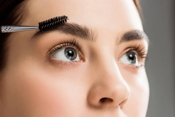 Abgeschnittene Ansicht der jungen Frau Styling Augenbraue mit Augenbrauenbürste auf grau — Stockfoto