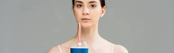 Панорамный снимок молодой женщины с проблемной кожей, держащей пластиковую чашку, изолированную на сером — стоковое фото