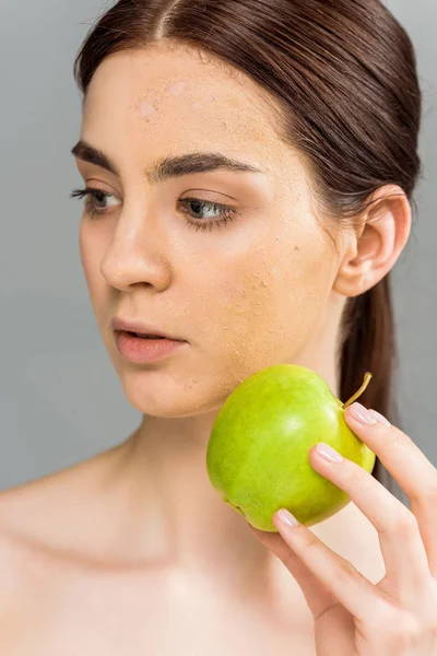 Jeune femme avec gommage du visage sur la peau tenant pomme isolée sur gris — Photo de stock