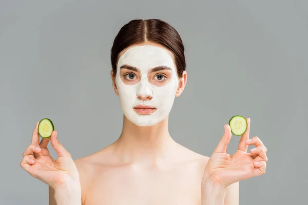 Giovane donna nuda con maschera di argilla sul viso tenendo cetrioli isolati su grigio — Foto stock