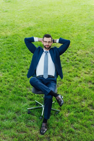 High angle view of businessman sitting in office chair in park with crossed lags and arms behind head — Stock Photo