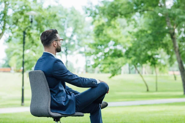 Giovane uomo d'affari seduto in sedia ufficio nel parco e in attesa — Foto stock