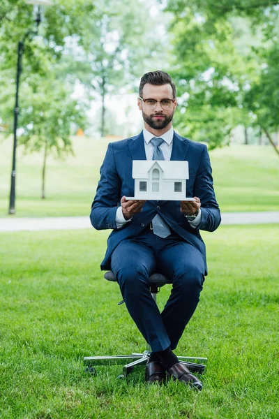 Вид в полный рост на молодого человека, держащего макет Белого дома и смотрящего на камеру, сидя в парке — стоковое фото