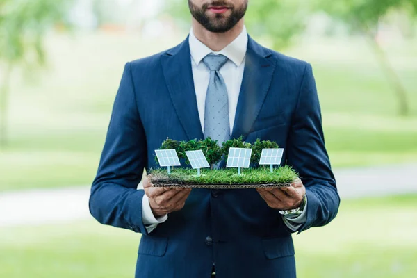 Vista recortada de un joven empresario sosteniendo el diseño del parque con baterías de sol mientras está de pie en el parque - foto de stock