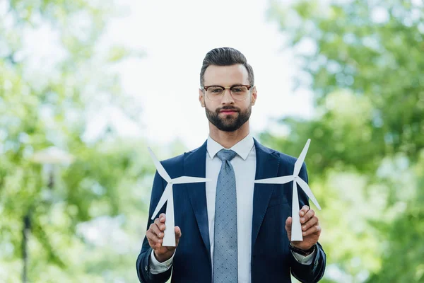 Young businessman holding windmills layout and looking at camera while standing in park — Stock Photo