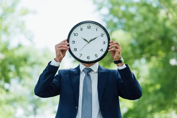 Young man covering face with clock while standing in park — Stock Photo