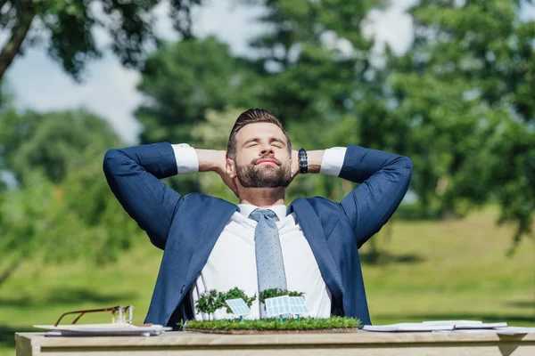 Jungunternehmer sitzt mit Sonnenbatterien am Tisch und entspannt mit den Händen hinter dem Kopf — Stockfoto