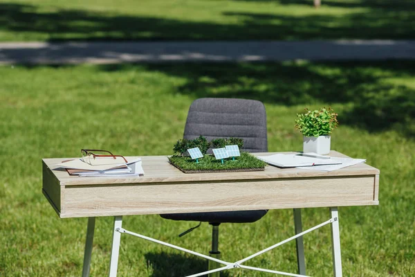 Table with sun batteries layout, flowepot, notebooks and glasses near office chair in park — Stock Photo