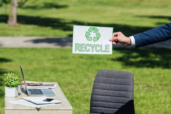Cropped view of businessman holding card with recycle sign near table in park — Stock Photo