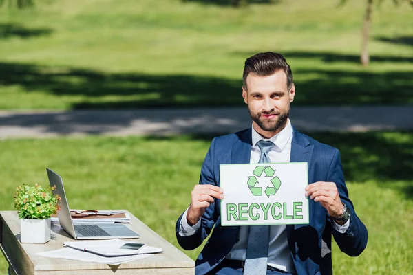 Geschäftsmann sitzt am Tisch und zeigt Karte mit Recycling-Schriftzug — Stockfoto