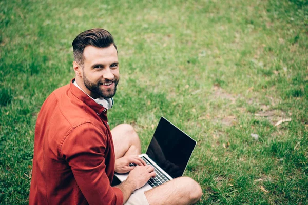 Homem de camisa vermelha usando laptop, sorrindo e olhando para a câmera — Fotografia de Stock