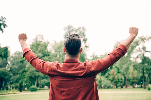 Back view of young man standing in park and putting hands in air — Stock Photo