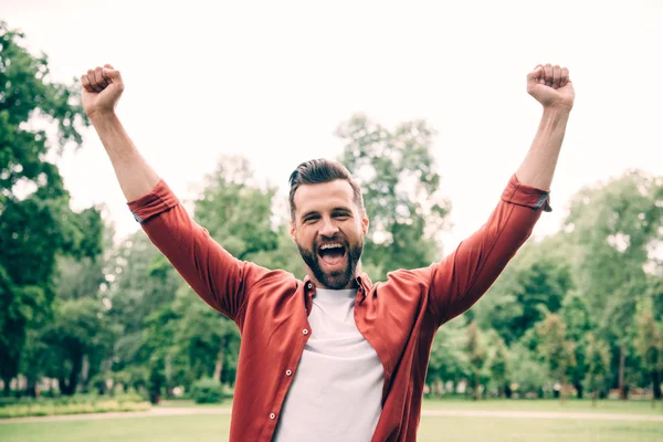 Excited young man standing in park and putting hands in air — Stock Photo