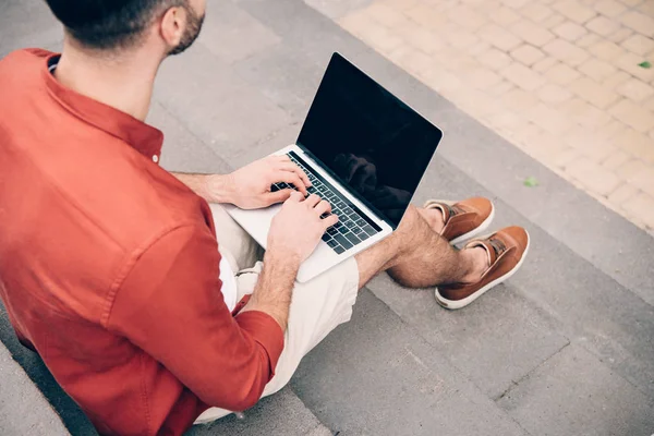 Vista ritagliata di giovane seduto su scale di pietra e utilizzando il computer portatile — Foto stock