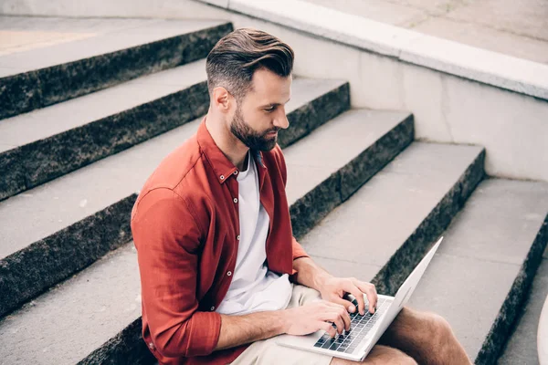 Jovem homem usando laptop enquanto sentado em escadas de pedra — Fotografia de Stock